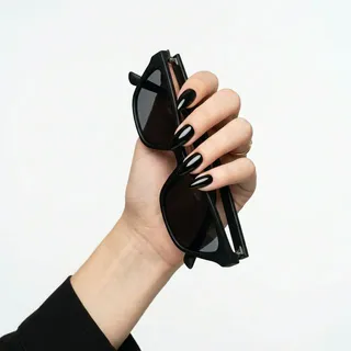 Glossy black ink stiletto nails holding minimalist black sunglasses frames