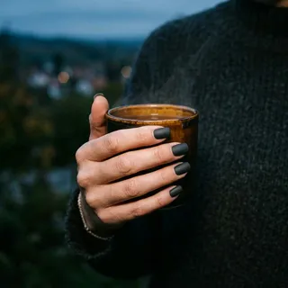 Matte charcoal grey square nails holding a hot mug outdoors at dusk